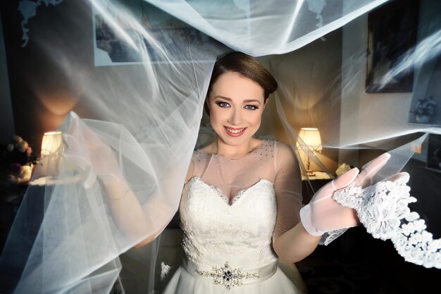 Photo portrait of happy beautiful bride standing amidst veil at home