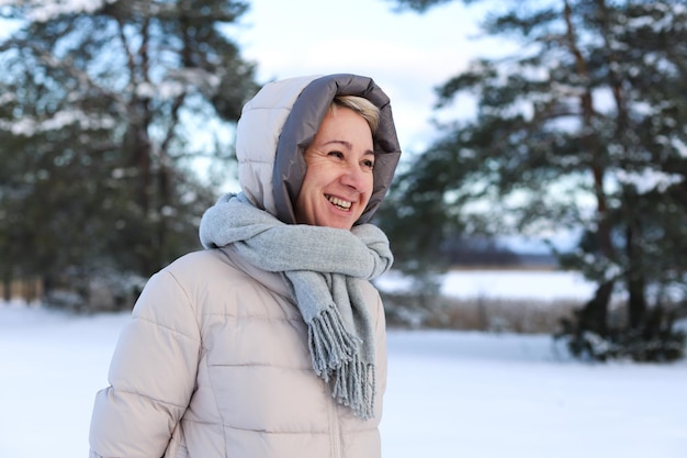 年齢の幸せな美しい年配の年配の引退した女性の肖像画は、冬の寒い日に笑顔で天気を楽しむ森や公園で屋外で雪を楽しんで遊んでいます。