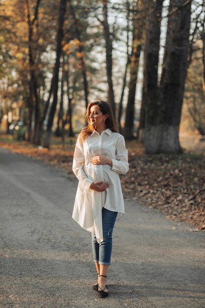 Portrait of a happy and beautiful pregnant woman looking at the light in the park at sunset The beauty of a woman during pregnancy How to be happy and healthy in autumn Autumn mood