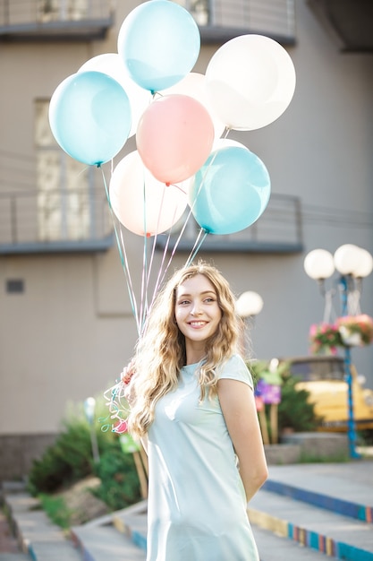 Portrait of happy beautiful woman with flying multicolored balloons in the city