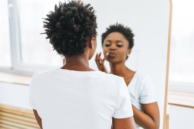 Portrait of happy beautiful young African American woman in white tshirt take make up against mirror