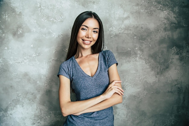 Portrait of happy beautiful young asian woman in t-shirt over concrete wall