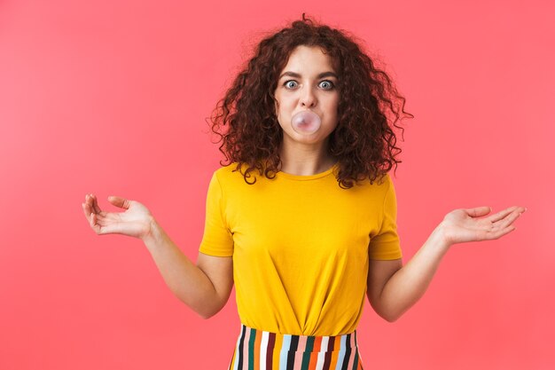 Portrait of a happy beautiful young curly woman posing isolated on red wall with bubble gum.