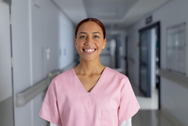 Portrait of happy biracial female doctor wearing scrubs in corridor at hospital