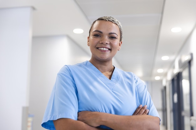 Foto ritratto di una donna medico bi-razziale felice con i capelli corti che indossa uno scrub nel corridoio dell'ospedale