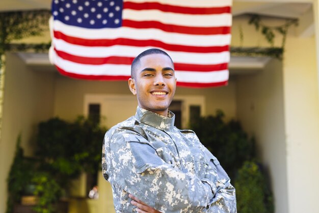 Photo portrait of happy biracial male american soldier wearing military uniform standing outside the house. american flag, patriotism and military service.