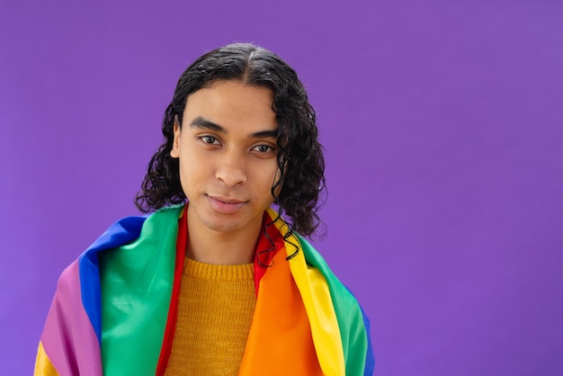 Photo portrait of happy biracial man holding lgbt rainbow flag and smiling on purple background. lgbt and pride concept.