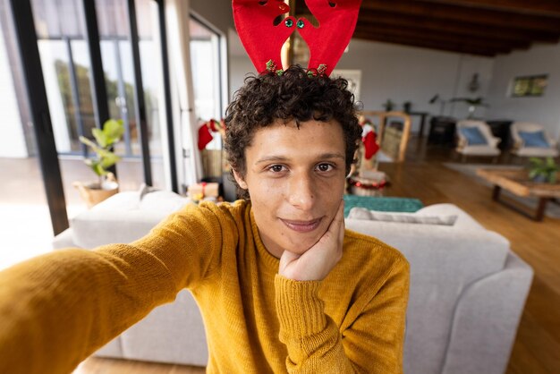 Portrait of happy biracial man wearing reindeer antlers and having video at christmas at home