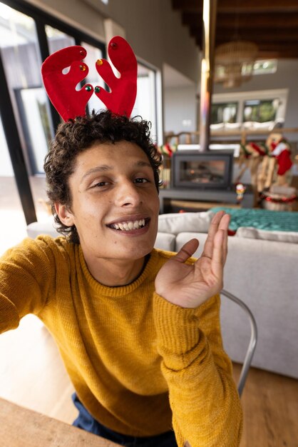 Foto ritratto di un uomo bi-razziale felice che indossa corna di renna e ha un video a natale a casa