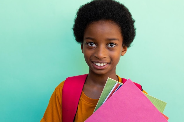 Portrait of happy biracial schoolboy with books wearing yellow tshirt over blue background