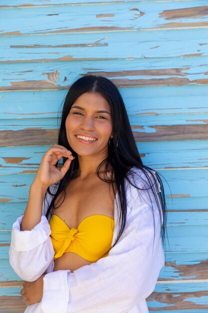 Photo portrait of happy biracial woman smiling to camera against weathered blue wooden boards. summer, beauty, wellbeing, free time, vacation and lifestyle, unaltered.