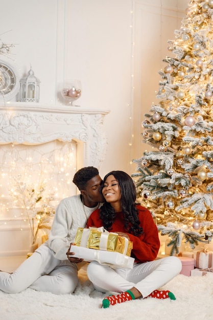 Portrait of happy black couple holding gifts and sitting near Christmas tree