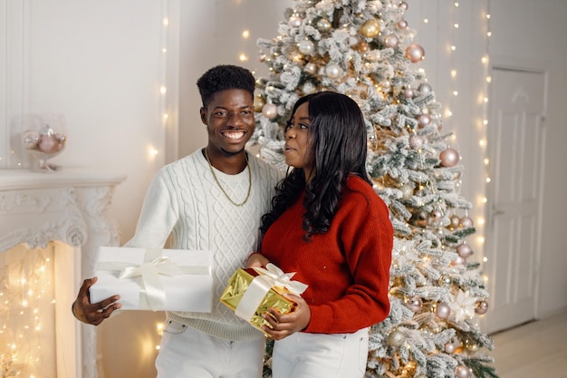 Portrait of happy black couple holding gifts and standing near Christmas tree