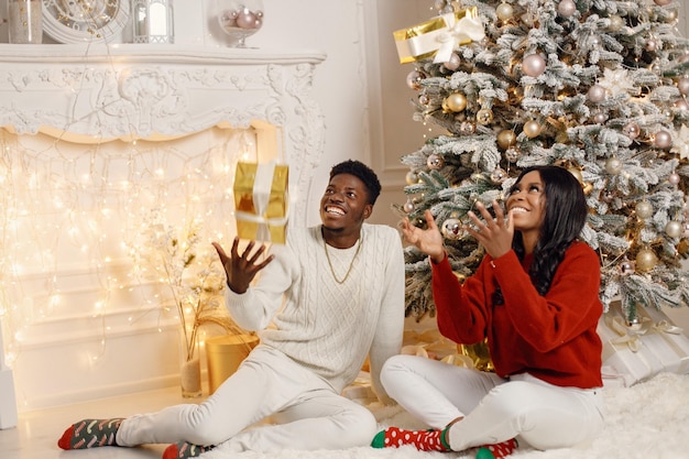 Portrait of happy black couple throwing gifts in the air while sitting near Christmas tree