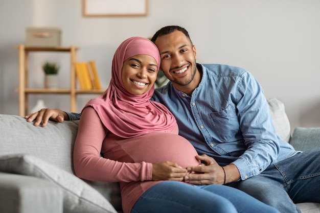 Portrait Of Happy Black Muslim Couple Expecting Baby Posing In Home Interior