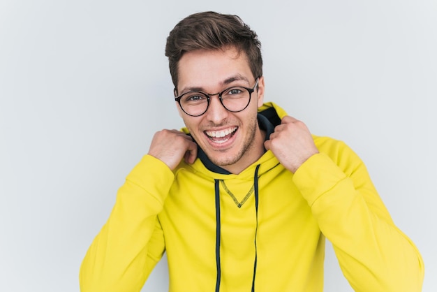 Portrait of happy blond wears yellow hoody and trendy glasses looks cheerful confidently into camera Young smiling student man posing against white studio wall People lifestyle and emotion concept