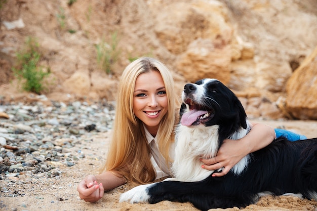 ビーチで彼女の犬を抱き締めて幸せな金髪の若い女性の肖像画