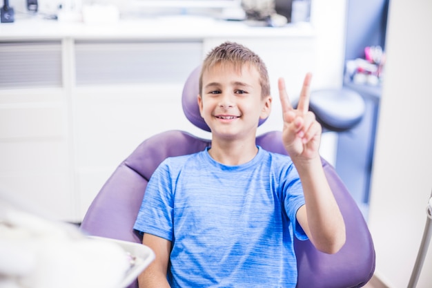 Photo portrait of a happy boy gesturing victory sign in clinic