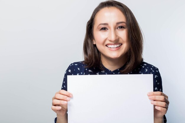 Portrait of happy brunette with advert looking at camera, Smiling woman holding white sign board. Casual dressed girl with advertising banner.