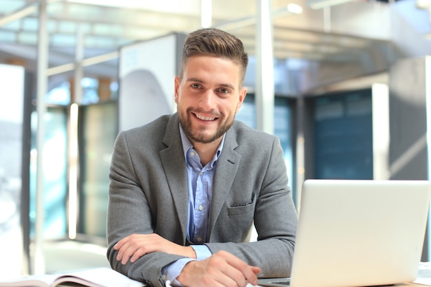 Portrait of happy businessman sitting at office desk, looking at camera smiling.