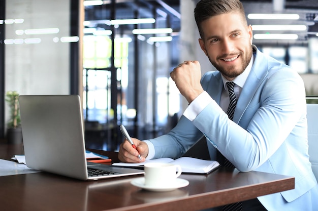 Portrait of happy businessman sitting at office desk looking at camera smiling