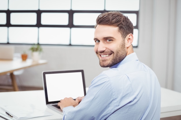 Portrait of happy businessman using laptop in office