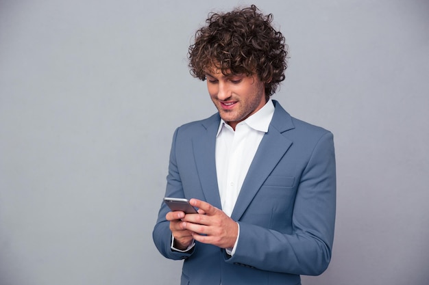 Portrait of a happy businessman using smartphone over gray wall