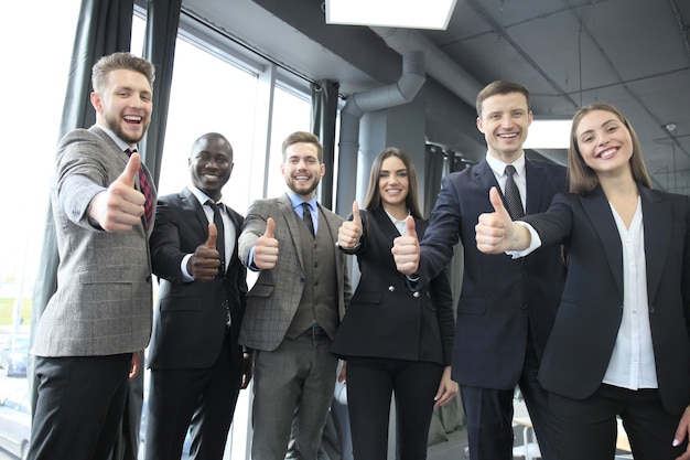 Portrait of happy businesspeople standing in office showing thumb up.