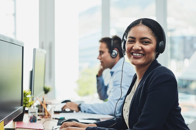 Portrait of happy call center agent working in a busy office assisting clients and providing good customer service Young smiling and cheerful professional excited to offer support or help on calls