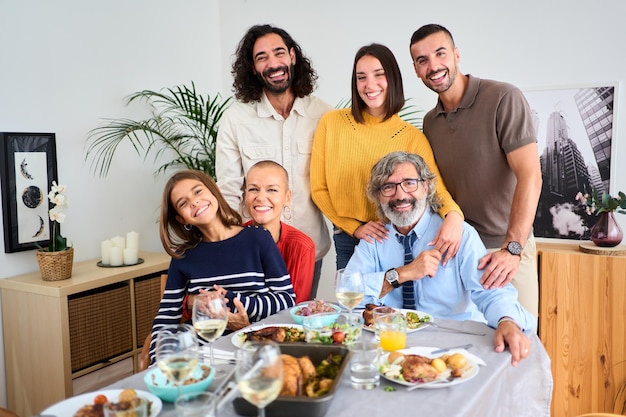 Portrait of happy caucasian family posing smiling looking at camera hugging around table indoors