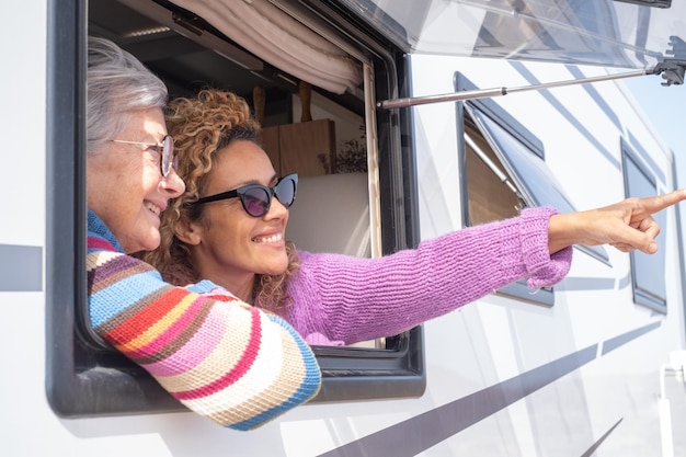 Portrait of happy caucasian friends women traveling in camper motor home looking out of the window