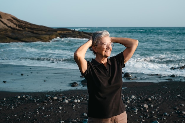 Ritratto di donna anziana caucasica felice in piedi su una spiaggia del mar nero al tramonto che distoglie lo sguardo donna anziana che si gode le vacanze o il pensionamento nel tempo libero