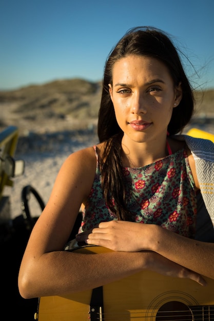 Portrait of happy caucasian woman on the beach holding guitar looking to camera. break on summer holiday road trip.