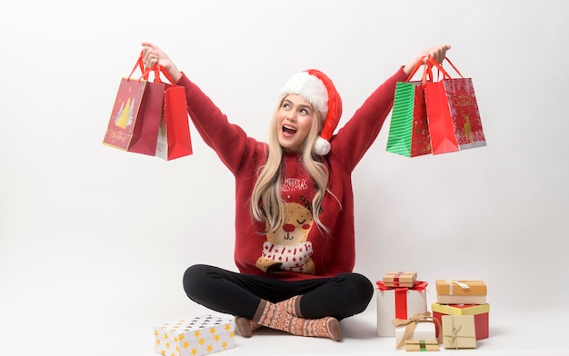Portrait of happy Caucasian young woman in santa claus hat with gift box and shopping bags