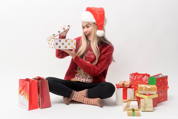 Portrait of happy Caucasian young woman in santa claus hat with gift box and shopping bags