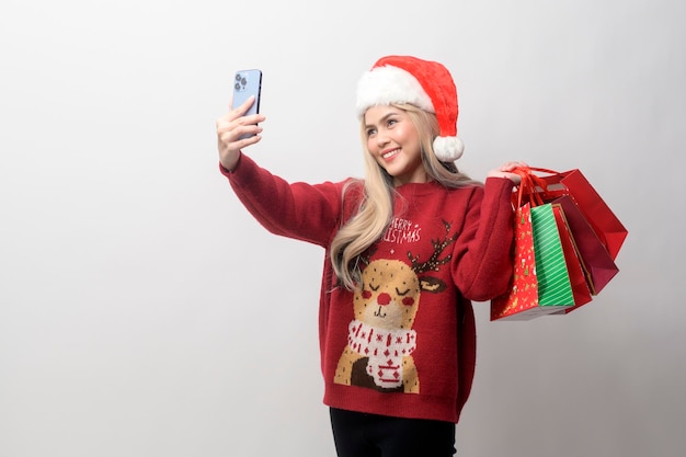 Ritratto di giovane donna caucasica felice in cappello di babbo natale con borse della spesa su sfondo bianco