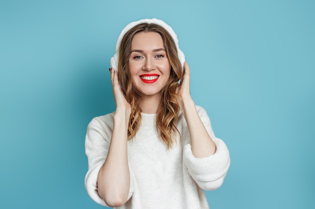 Ritratto di una giovane donna caucasica felice in cuffie di pelliccia invernale in un maglione bianco sorridente