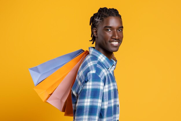Photo portrait of happy cheerful black man holding lots of bright shopping bags