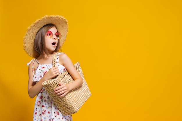 Portrait of happy cheerful girl in summer hat sunglasses straw bag over yellow background