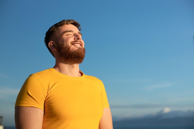 幸せな陽気なポジティブな男の肖像ひげを生やした若いハンサムなひげを生やした男の肖像は、晴れた日を楽しんでいます