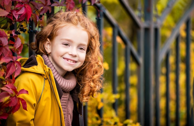Портрет счастливой веселой рыжеволосой кудрявой девочки-подростка на природе среди яркого осеннего леса