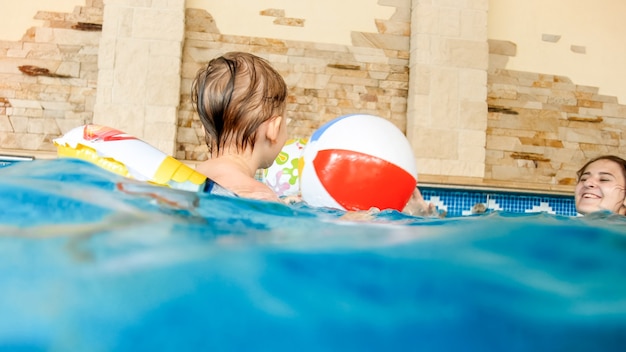 Portrait of happy cheerful toddler boy playing with inflatable\
beach ball and colorful ring at indoor swimming pool in house