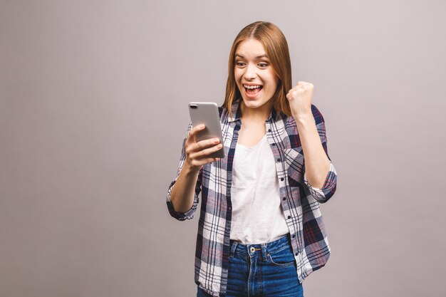 Ritratto di una donna allegra felice che celebra successo stando in piedi e guardando il telefono cellulare.
