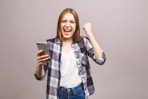 Ritratto di una donna allegra felice che celebra successo stando in piedi e guardando il telefono cellulare.