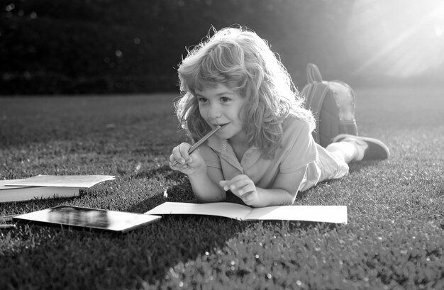 Portrait of happy child boy with book in park kids early education little kid with pencil writing on