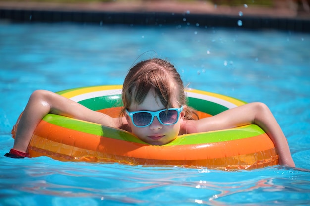 熱帯の休暇中の晴れた夏の日にプールで膨脹可能な円でリラックスする幸せな子供の女の子の肖像画夏の活動の概念