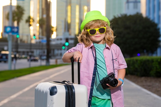 Portrait of happy child traveler with luggage Positive little tourist with suitcase ready to travelling Happy kid tourist with baggage going to travel on holidays
