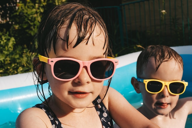 夏の暑い日にプールでサングラスをかぶった幸せな子供たちの肖像画