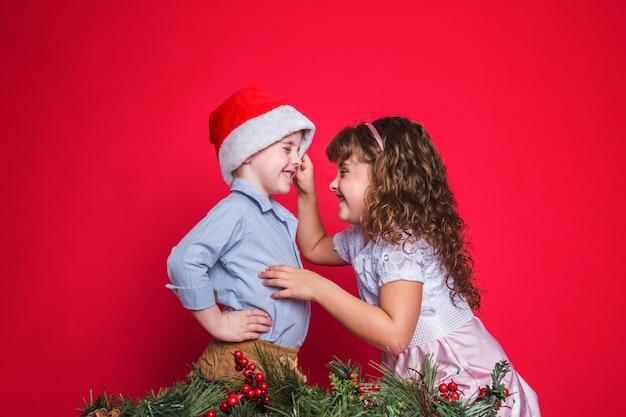 Ritratto di bambini felici con cappello di babbo natale su sfondo rosso.