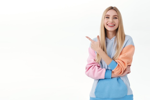 Portrait of happy, confident good-looking blond girl pointing finger left and smiling